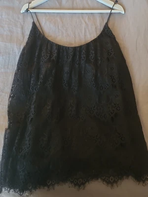 Svart spetslinnetopp med tunna band - Säljer en svart linnetopp med tunna axelband och spets över hela toppen ifrån Gina Tricot. Toppen har en lös passform och spetsdetaljer längs nederkanten.