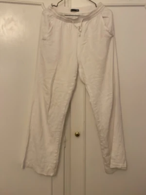 Vita linnebyxor med resårmidja - Säljer ett par vita linnebyxor med avslappnad passform och resår i midjan. Byxorna har snedställda fickor fram och en bakficka. Perfekta för en chill och luftig stil. Materialet är linne som ger en skön känsla.