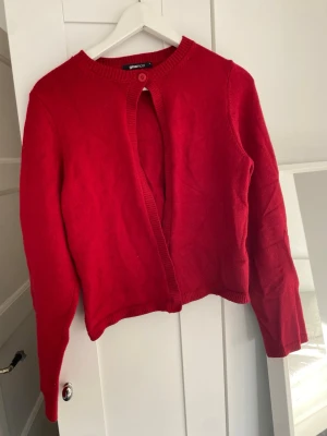 Röd kofta från Gina Tricot - Snygg röd kofta från Gina Tricot med rund halsringning och ribbade kanter. Koftan har en enkel knapp framtill och är tillverkad i mjukt stickat material. Perfekt att slänga över en topp för en chill look. Koftan är i mycket bra skick och har endast använd 1 gång. 