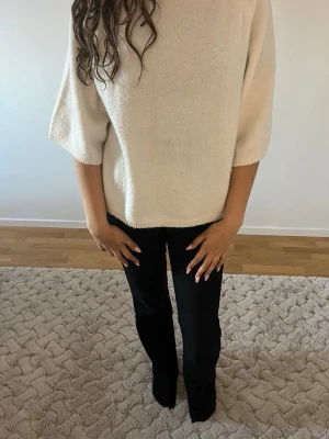 Beige stickad tröja med halvlånga ärmar - Säljer en enkel och stilren beige stickad tröja med halvlånga ärmar och rund halsringning. Tröjan har en rak passform och är perfekt för lager på lager. Materialet ser mjukt och bekvämt ut, perfekt för dig som gillar en clean look.