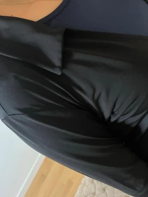 Svart knytkofta med långa ärmar - Snygg svart kofta med knytning framtill och långa ärmar. Koftan har en mjuk och följsam passform, perfekt att slänga över ett linne eller topp. Enkel och stilren design som passar till många olika outfits.