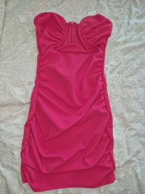 Rosa axelbandslös klänning Gina Tricot - Säljer en snygg rosa axelbandslös klänning från Gina Tricot. Klänningen är kort och har en draperad design med rynkade detaljer och en söt hjärtformad urringning. Perfekt för dig som vill sticka ut med en färgstark look. Lite nött under brösten, se sista bilden, inget man igentligen tänker på😍🌺