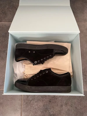 Svarta sneakers från Lanvin - Stilrena svarta sneakers från Lanvin med en mix av mocka och lackdetaljer. Skorna har lågt skaft, svarta skosnören och metallfärgade öljetter. Perfekta för dig som gillar en clean och lyxig look. Vid snabb affär kan jag gå ner i pris! Kan även putsa till och rena de lite innan jag fraktar dem. Hör av er vid frågor!
