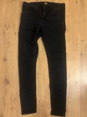 Svarta skinny malone jeans från Lee - Snygga svarta skinny jeans från Lee med klassisk femficksdesign och smal passform. Jeansen har en enkel look utan slitningar och är tillverkade i ett stretchigt material som sitter tajt längs benen. Perfekta för en clean och stilren outfit.