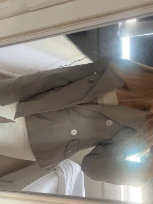 Grå kavaj med stora knappar - Snygg grå kappa med stora dekorativa knappar och klassisk krage. Rak passform och enkel design som passar till många olika stilar. Perfekt att matcha med både jeans och kjol 