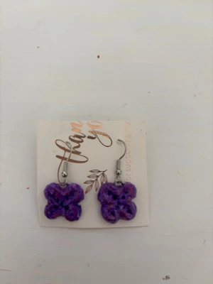 Lila handgjorda blomörhängen - Unika örhängen i form av lila blommor, handgjorda i lera. De har krokfästen i metall och en glansig finish. Perfekta för dig som vill ha något färgglatt och personligt i din stil.