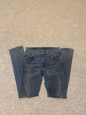 Blåa jeans från Nudie - Snygga blå jeans från Nudie. Jeansen har diskreta slitningar framtill och är tillverkade i denim med en autentisk tvättad look. Perfekta för en avslappnad och stilren outfit.