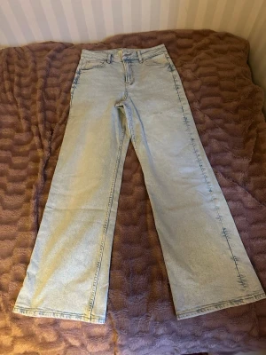 Ljusblåa raka jeans med hög midja Gina Tricot - Säljer ett par ljusblå jeans med rak passform och hög midja. Jeansen har klassiska fem fickor och stängs med dragkedja och knapp. Materialet är denim i bomull och de har en avslappnad, trendig look som passar perfekt till vardagsstilen.