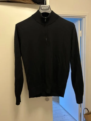 Svart stickad tröja med halvzip Uniqlo - Snygg svart stickad tröja från Uniqlo med halvzip och hög krage. Tröjan har långa ärmar och ribbade muddar vid ärmslut och nederkant. Perfekt för lager på lager och enkel att matcha med olika outfits.