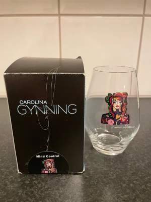 Carolina Gynning glas Mind Control - Dricks glas från Carolina Gynning med färgstarkt konstmotiv 'Mind Control'. Glaset har en modern form och motivet är tryckt i flera starka färger som rött, grönt och lila. Perfekt för dig som gillar konstnärliga detaljer i hemmet. Levereras i originalförpackning.