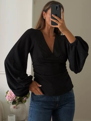 Svart v-ringad topp från NA-KD - Trendig svart topp från Na-KD med v-ringning och långa puffärmar. Toppen har en figurnära passform med rynkade detaljer i midjan och är tillverkad i ett strukturerat, mjukt material. Perfekt att styla med jeans eller kjol för en snygg look.