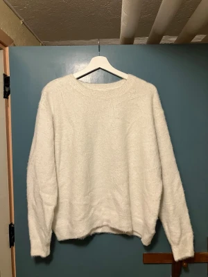 Vit fluffig stickad tröja H&M - Mysig vit stickad tröja från H&M i storlek M. Tröjan har en fluffig och mjuk känsla, rund halsringning och långa ärmar. Perfekt för att hålla värmen under kyliga dagar och enkel att matcha med olika outfits.