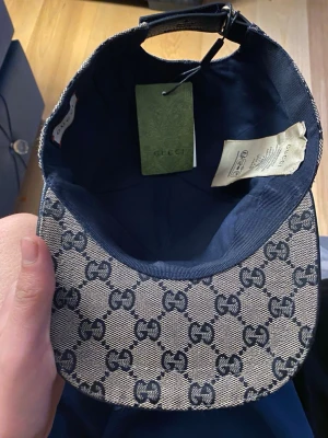 Gucci keps  - Säljer en snygg keps från Gucci med klassiskt GG-monogram i blått och beige. Kepsen har justerbart band bak i svart läder och är tillverkad i canvasmaterial. Perfekt för dig som vill ha en stilren accessoar med lyxig känsla.