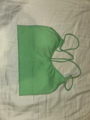 Grön ribbad bralette med smala band - Snygg grön bralette med ribbad struktur och tunna axelband som korsas i ryggen. Mjuk och stretchig modell utan bygel, perfekt för en avslappnad och trendig look. Materialet känns lent mot huden och ger bra stöd. Märke och storlek saknas.