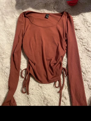 Rostbrun ribbad topp från SHEIN - Trendig rostbrun långärmad topp från SHEIN med ribbad struktur och snörning i sidorna. Toppen har en rundad urringning och croppad passform som ger en snygg siluett. Perfekt att styla med höga jeans eller kjol.