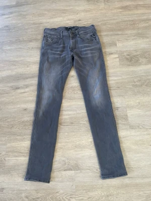 Replay grå slim fit jeans - Säljer ett par grå slim fit jeans från Replay med snygga slitningar och klassisk femficksdesign. Jeansen har Replay-logga på myntfickan och är tillverkade i ett stretchigt material för skön passform. Perfekta för en avslappnad och trendig look.