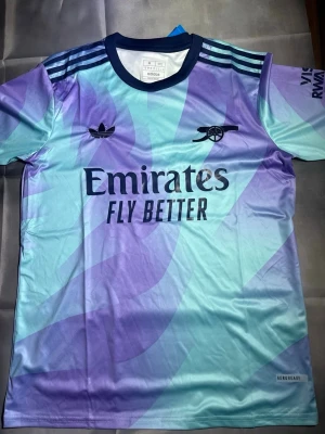 Arsenal tröja - Snygg Arsenal matchtröja från Adidas med lila och blått mönster, mörkblå detaljer och klubbens logga på bröstet. Perfekt till sommaren. Storlek M men passar S också. Skriv vid funderingar och pris kan dirkuteras vid snabb affär.