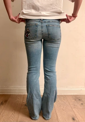 Bootcut ljusblå jeans med tigerpatch - Innerbenslängd: 78 cm                                 Midjemått rakt över: 35 cm                       Grenlängd: 19 cm                                     Benöppning: 22 cm