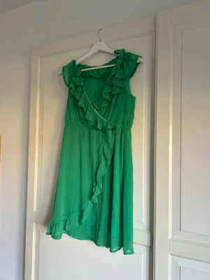 Grön omlottklänning med volang - Grön omlottklänning med volangdetaljer längs urringningen och nederkanten!! En härlig sommarklänning!!💚