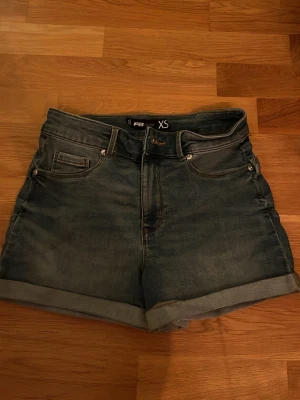 Blåa denimshorts hög midja XS - Säljer ett par klassiska blåa denimshorts från F&F i storlek XS. Shortsen har hög midja, fem fickor och uppvikta benslut för en chill look. Perfekta till sommaren och lätta att matcha med allt.