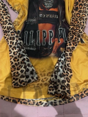 Leopardmönstrad topp Philipp Plein - Cool långärmad topp från Philipp Plein med leopardmönstrade ärmar och detaljer, samt tryck framtill med glittriga stenar och text. Basen är gul med leoparddetaljer och ett stort motiv på bröstet. Perfekt för dig som gillar statement-plagg.