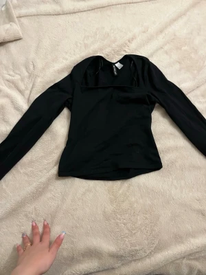 Svart långärmad topp från H&M Divided - Snygg svart långärmad topp från H&M Divided med fyrkantig urringning. Toppen har en tight passform och är tillverkad i mjukt material som känns skönt mot huden. Perfekt att styla med jeans eller kjol för en trendig look.