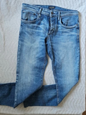 Blå slim fit jeans från Jack & Jones - Säljer ett par ljusblå slim fit jeans från Jack & Jones med klassisk femficksdesign och snygga slitningar. Jeansen har normal midja och dragkedjegylf. Perfekta för en avslappnad och trendig look.