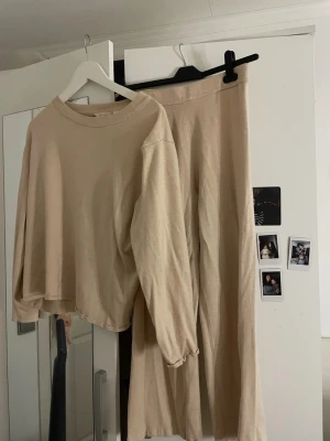 Beige loungewear set med vida byxor - Mysigt loungewear set i beige med långärmad tröja och matchande vida byxor. Tröjan har rund halsringning och avslappnad passform, byxorna har resår i midjan och är vida i benen. Perfekt för chill dagar hemma. Byxorna är i st S och tröjan i M 😊