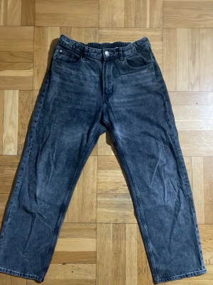 Svarta Loose-Fit Jeans  med tvättad look - Säljer ett par svarta jeans med tvättad vintage-look och raka ben. Jeansen har klassisk femficksmodell, knappgylf och normal midja. Materialet är denim i bomull och de har en avslappnad passform som passar till det mesta.