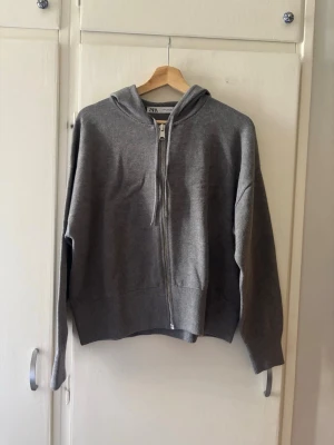 Grå zip hoodie från Zara - En stilren grå hoodie från Zara med dragkedja framtill och huva. Tillverkad i mjukt sweatshirtmaterial som känns skönt mot huden. Perfekt för en avslappnad look och enkel att matcha med jeans eller joggers.