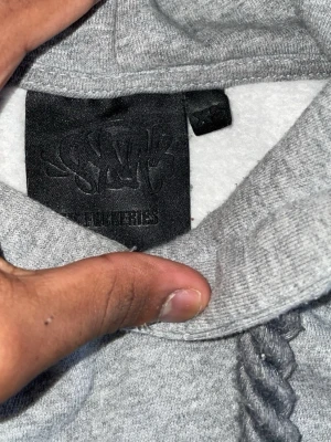 Grå hoodie syna world - Snygg grå hoodie från syna world med klassisk huva och dragsko. Tillverkad i mjukt sweatshirtmaterial som känns skönt mot huden. Perfekt för dig som gillar en enkel och clean stil. Passar till det mesta och är lätt att matcha med andra plagg.