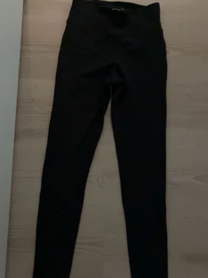 Svarta leggings från New Apparel XS - Säljer ett par svarta leggings från New Apparel i storlek XS (32/34). De har en hög midja och är tillverkade i ett stretchigt material som sitter tajt längs benen. Perfekta för en enkel och clean look.