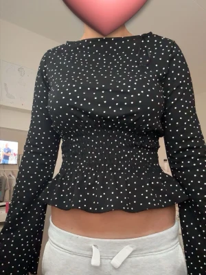 Svart prickig blus med volang - Snygg svart blus med vita prickar och smockad midja som ger en figurnära passform. blusen är i Xs och knappt använd.