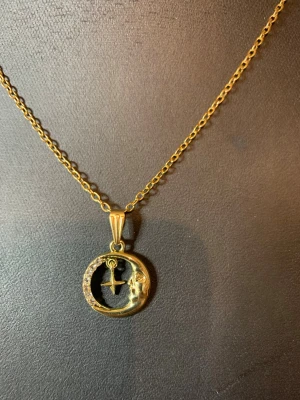 Guldhalsband med måne och stjärna - Unikt halsband i guldfärgad metall med ett runt hänge som har en måne och en hängande stjärna i mitten. Månen är dekorerad med små gnistrande stenar för extra bling. Perfekt för dig som gillar detaljerade och personliga smycken.