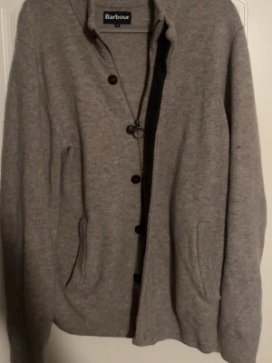 Barbour cardigan  - Mysig grå kofta från Barbour. Finns en liten defekt på ryggen som ni ser på sista bilden. Annars i väldigt bra skick. Köpte i Barbour afären i Stockholm ny pris 1800kr kom gärna med frågor och funderingar🫡