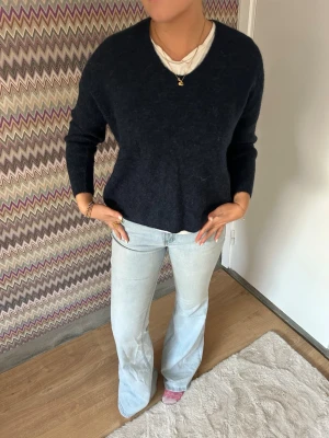 Mörkblå fluffig V-ringad tröja från mos mosh - Mysig mörkblå tröja med V-ringning och lång ärm. Tröjan har en fluffig, mjuk struktur och avslappnad passform. Perfekt att bära över en t-shirt för en enkel men snygg look. Från mosmosh