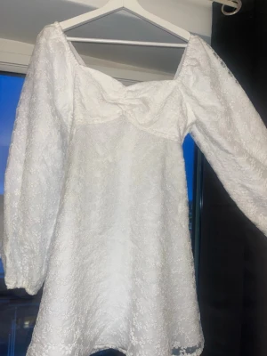 Vit spetsklänning med puffärm - Supersöt vit kortklänning med långa puffärmar och v-ringad byst. Klänningen är täckt av blommig spets och har en feminin, romantisk look. Perfekt för sommarens alla tillfällen och ger en riktigt fräsch vibe. Perfekt klänning till student, där jag själv hade på mig den under motatagningen! 