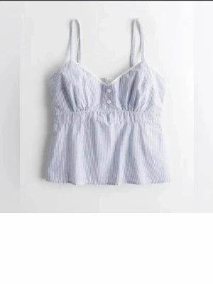 Blåvit randig linnetopp - Snygg blåvit randig linnetopp med tunna axelband och två knappar framtill. Toppen har en lätt rynkad midja och är tillverkad i ett tunt, luftigt bomullsmaterial. Perfekt för varma dagar och enkel att styla med jeans eller kjol. lappen är borta, så kan icke se vad märken eller stoleken är men skulle tippa på s! 