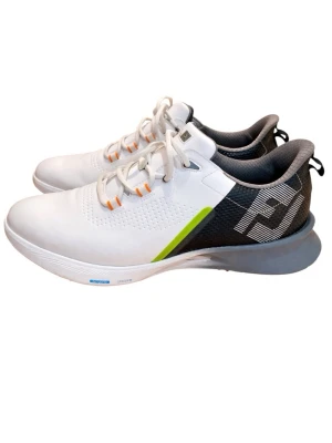 Vita FootJoy golfskor med färgdetaljer - Snygga vita golfskor från FootJoy med svart och grå häl, limegrön detalj och orange inslag vid snörningen. Yttersulan har orange och blå partier med greppvänlig struktur. Ovandelen är i syntetmaterial och skon har en sportig, modern look.