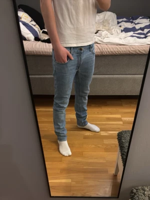Ljusblå slim fit jeans - Säljer ett par ljusblå slim fit jeans med klassisk femficksdesign och normal midja. Jeansen har en modern passform som sitter snyggt längs benen och är perfekta för en avslappnad stil. Materialet är mjukt denim som ger bra komfort.
