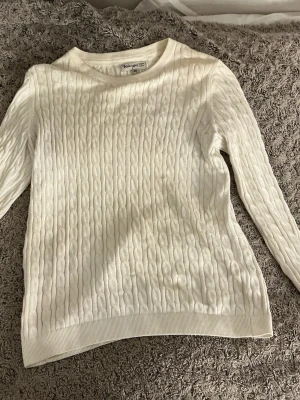 Vit kabelstickad tröja Basic You - Kabelstickad vit tröja från Basic You i ekologisk bomull. Tröjan har rund halsringning, långa ärmar och ribbade muddar vid ärmslut och nederkant. Perfekt för dig som gillar en clean och klassisk look.