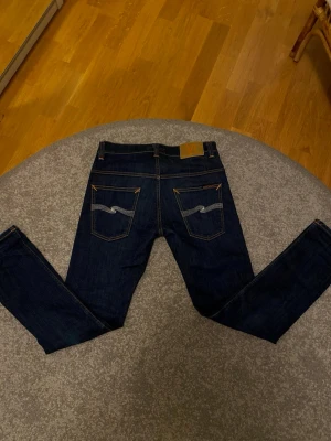 Mörkblåa Nudie jeans - Säljer ett par riktigt schyssta Nudie jeans i storlek W30 L30 och de är i ny skick. Det är sytt med orange tråd vilket ger byxor ett unik och skitsnygg still. 