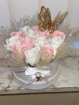 Evighetsrosor presentbox med fjäril - Säljer en Rosbox i vitt med pärldetaljer och fin logga, fylld med konstgjorda rosor i vitt och ljusrosa. Ovanpå sitter en stor guldfärgad fjäril och skimrande tyll med guldprickar. Perfekt som inredningsdetalj eller present.