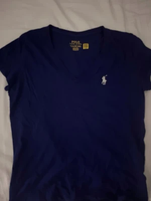 Marinblå v-ringad t-shirt Polo Ralph Lauren - Snygg marinblå t-shirt från Polo Ralph Lauren med klassisk v-ringning och den ikoniska vita logobrodyr på bröstet. Tillverkad i mjuk bomull som känns skön mot huden. Perfekt för en clean och stilren look.