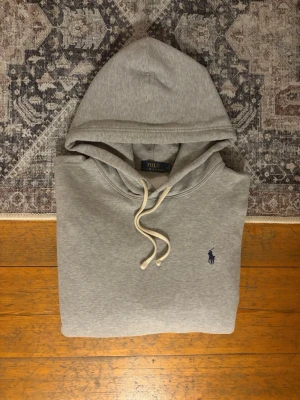 Polo Ralph Lauren Flecce Hoodie Storlek L - Hej!👋  Säljer en ljusgrå Polo Ralph Lauren Fleece Hoodie. Hoodien är i mycket gott skick, men har en mycket liten mörkare prick på magfickan. Den är original och har en qr kod som man kan skanna.  Storlek: L i herr, 180/100A. Mått skickas privat😀 Skickar snabbt!🚛📦 Hör av er vid frågor💯