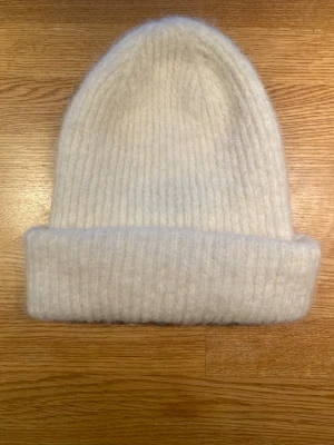 Vit ribbstickad mössa från Pieces - Mysig vit ribbstickad mössa från Pieces i one size. Tillverkad i ett fluffigt och mjukt material som håller dig varm. Klassisk modell med uppvikt kant som ger en clean och stilren look. Pieces ny vit mössa modell pcbera wool hood noos  Ny, aldrig använd   One Size  52% polyester, 38% akryl, 8% ull och 2% elastan  Kommer från ett djur och rökfritt hem