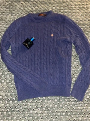 Lila kabelstickad tröja från Morris - Snygg lila kabelstickad tröja från Morris i 100% bomull. Tröjan har rund halsringning, ribbade muddar och en liten broderad logga på bröstet. Perfekt för dig som gillar klassisk och stilren design.