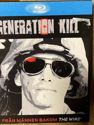 Generation Kill Blu-ray box - Säljer en Blu-ray box av Generation Kill, en verklighetsbaserad miniserie om USA:s invasion av Irak. Boxen innehåller 3 skivor med 7 avsnitt och över 7 timmars speltid. Omslaget är svart och grått med vita och röda detaljer. Inkluderar extramaterial och interaktiva funktioner.