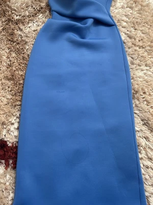 Blå långkläning slät polyester - En stilren blå långkläning  med rak passform och slät yta. Kjolen är enkel och minimalistisk utan synliga detaljer eller mönster, vilket gör den lätt att matcha med olika toppar. Tillverkad i ett mjukt polyestertyg som ger ett snyggt fall.