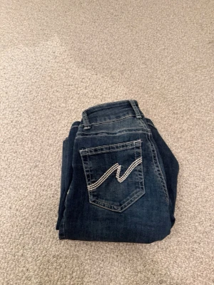 Mörkblå bootcut jeans med broderad ficka - Säljer ett par jeans från Nelly, storlek 32. Bra skick knappast använt. Strechigt material och super sköna!💕